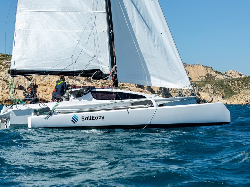 Starboard / right side of Tricat 30 sailing in front of rocky shoreline