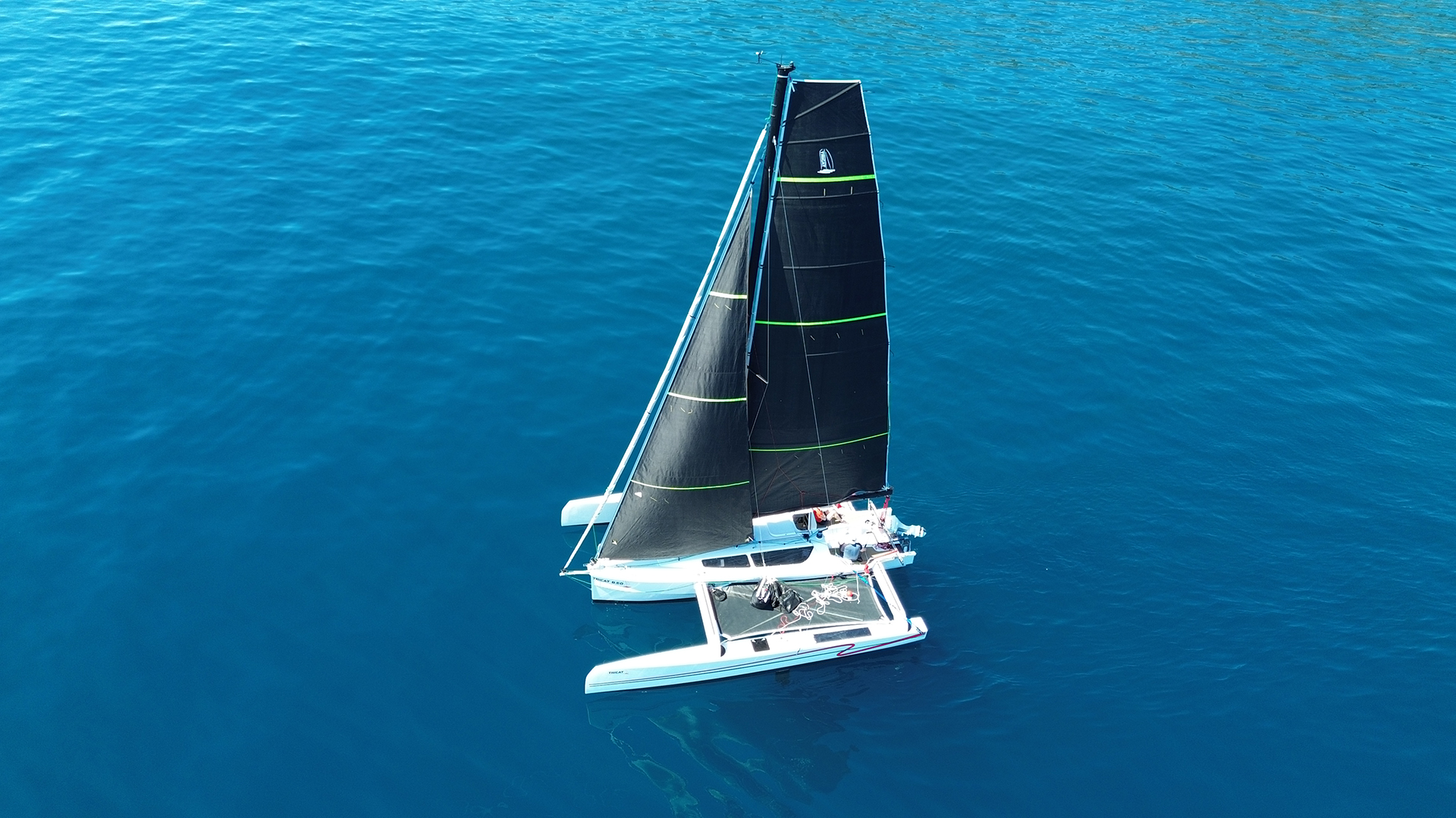 Tricat 8.50 sailing in light winds. White hull, black sails and incredibly blue water.